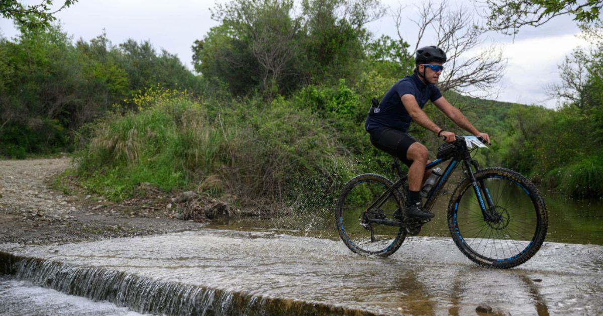 Cyclist riding a gravel backroad through a river ford near Megalopolis, Arcadia